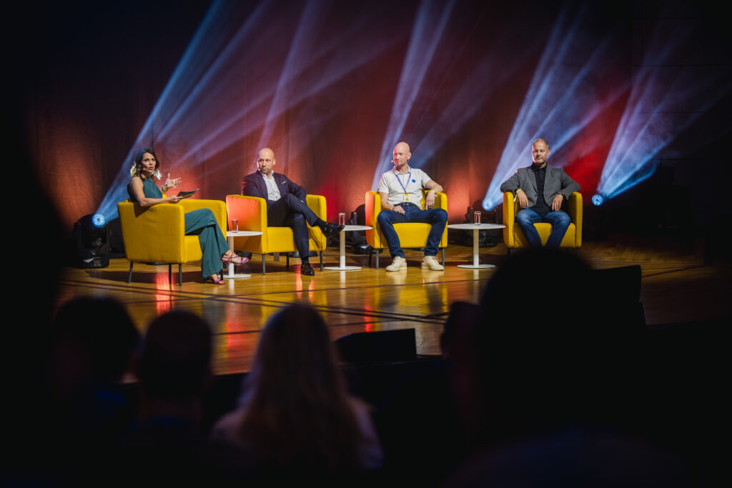 Konferenz Moderatorin Franziska Zimmermann moderiert einen Panel Talk mit 3 Teilnehmern auf einer großen Konferenz
