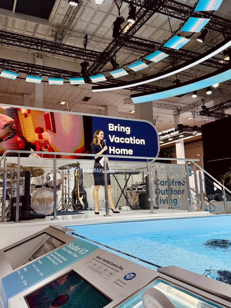 Messe Moderatorin in blauem Kleid auf großer Messebühne mit Pool davor
